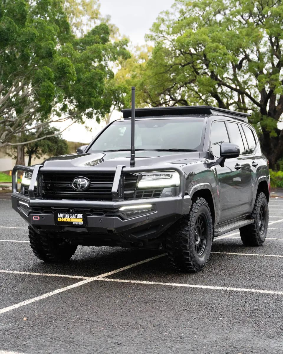 Toyota LandCruiser VX 300 Series in grey with ARB bull bar, snorkel, roof rack, and mud tyres in a car park.