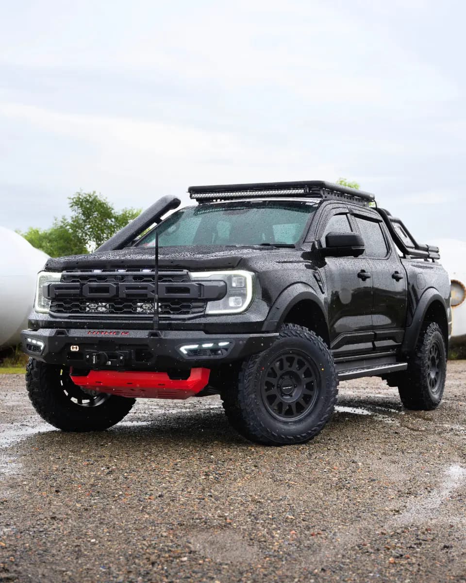 Ford Ranger Raptor in black with Hamer bull bar, red skid plate, roof rack, and snorkel on wet gravel.