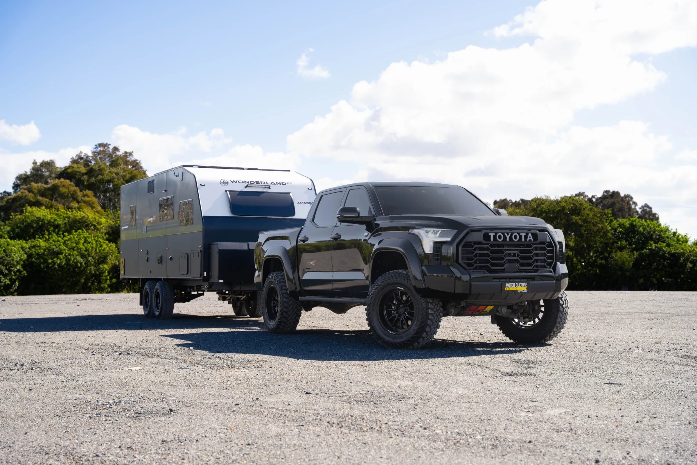 Black lifted 2024 Toyota Tundra Limited hitched to the 2026 Wonderland RV Amaroo 2106 off-road caravan on gravel under a blue sky.