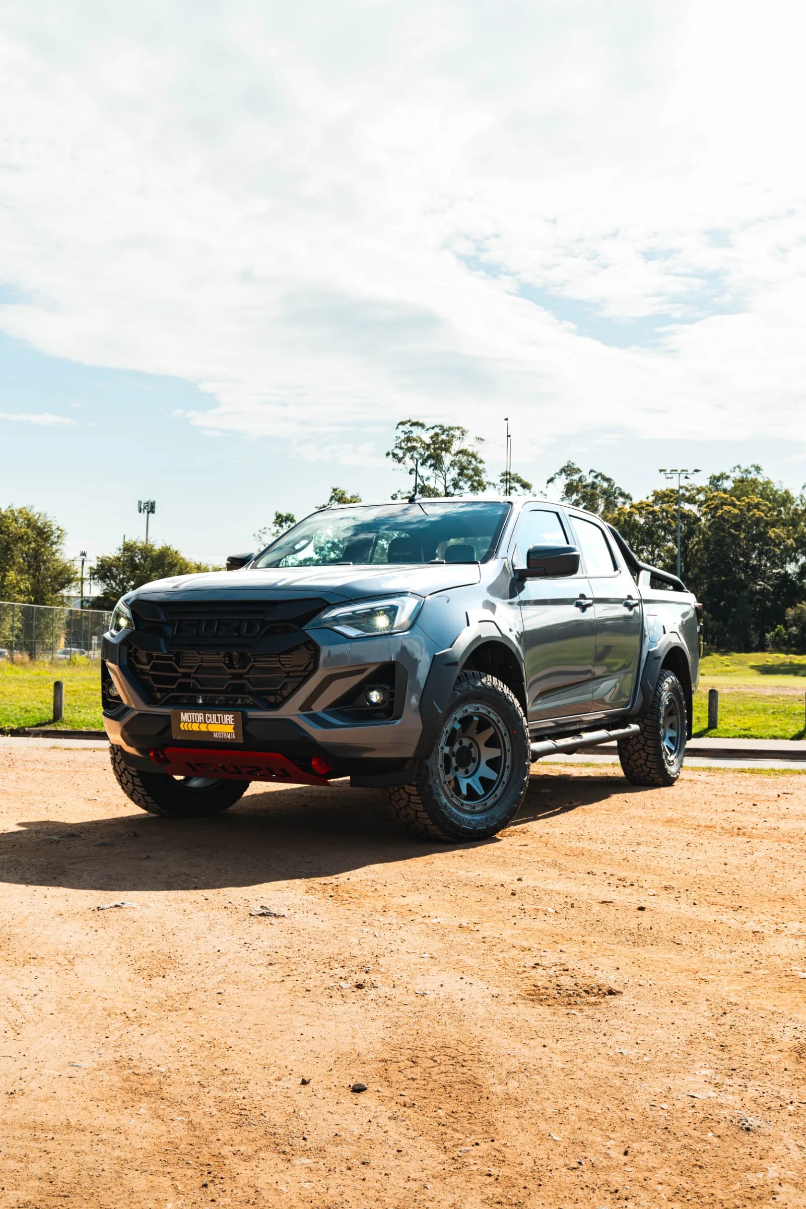 Isuzu D-MAX BLADE in grey parked on dirt, front three-quarter view with red underbody accents.