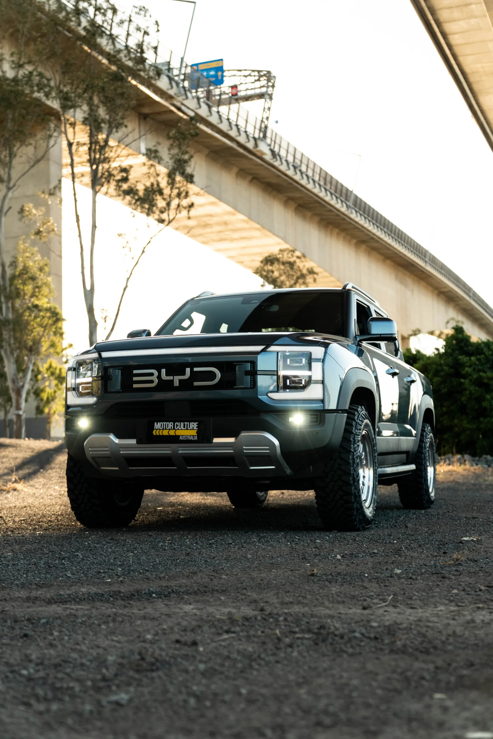 BYD Shark 6 Premium dark ute front view with fog lights on under overpass.