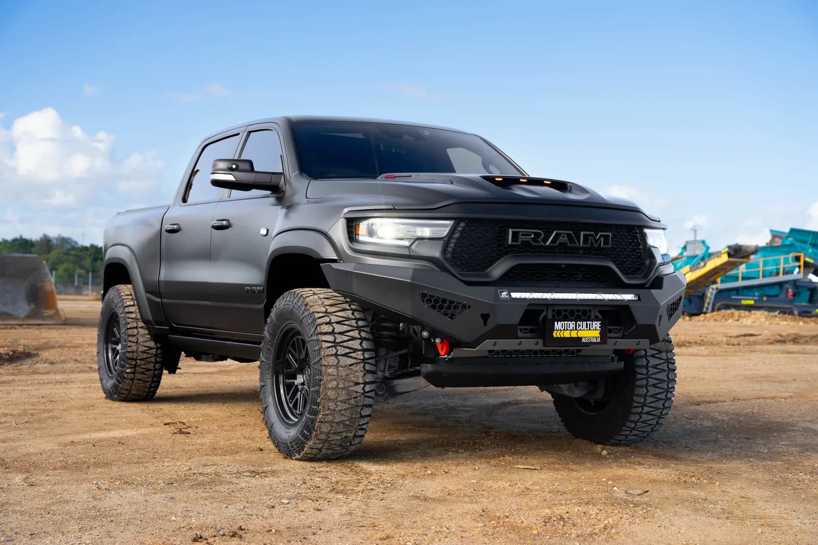 Satin grey RAM 1500 TRX with bullbar and aftermarket wheels parked on a worksite, front three-quarter view